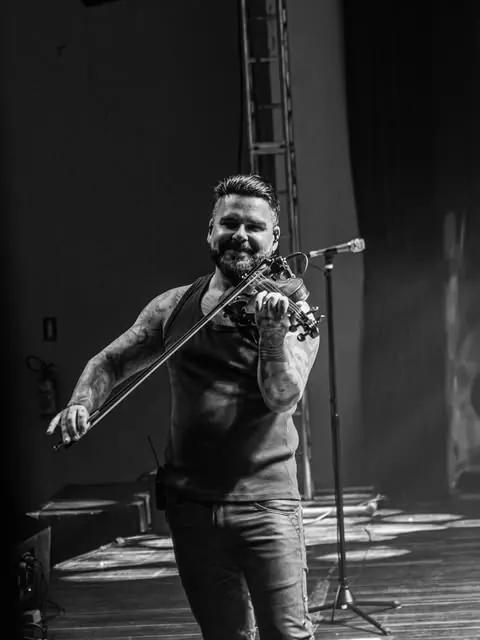 Violinista sorrindo enquanto toca no palco, em preto e branco