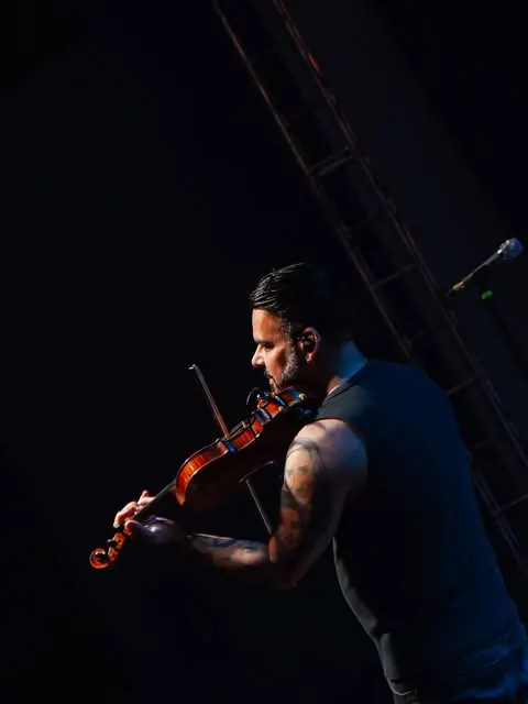 Violinista tocando em meio à penumbra do palco